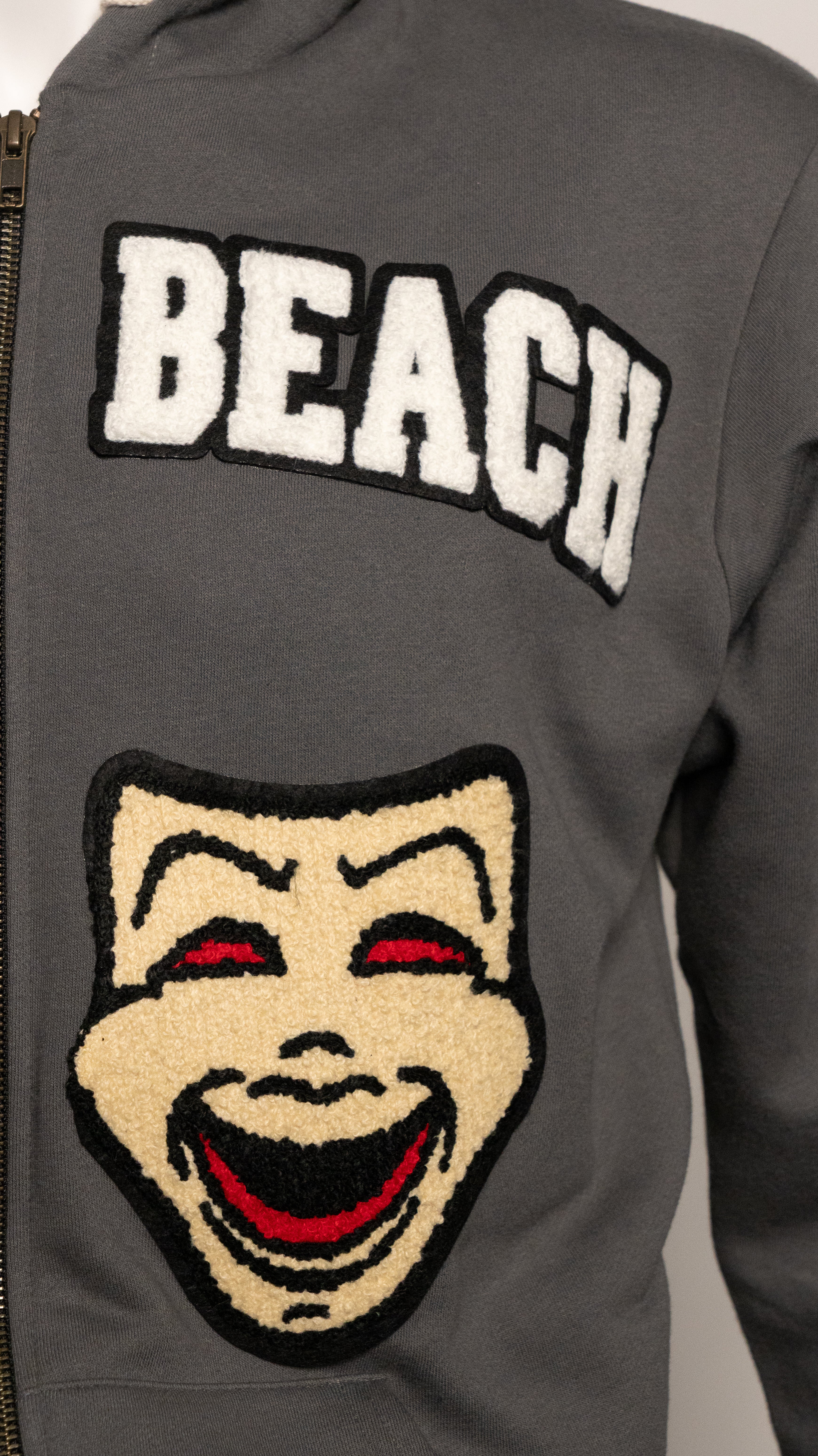 Gray jacket with 'BEACH' text and a laughing face patch.