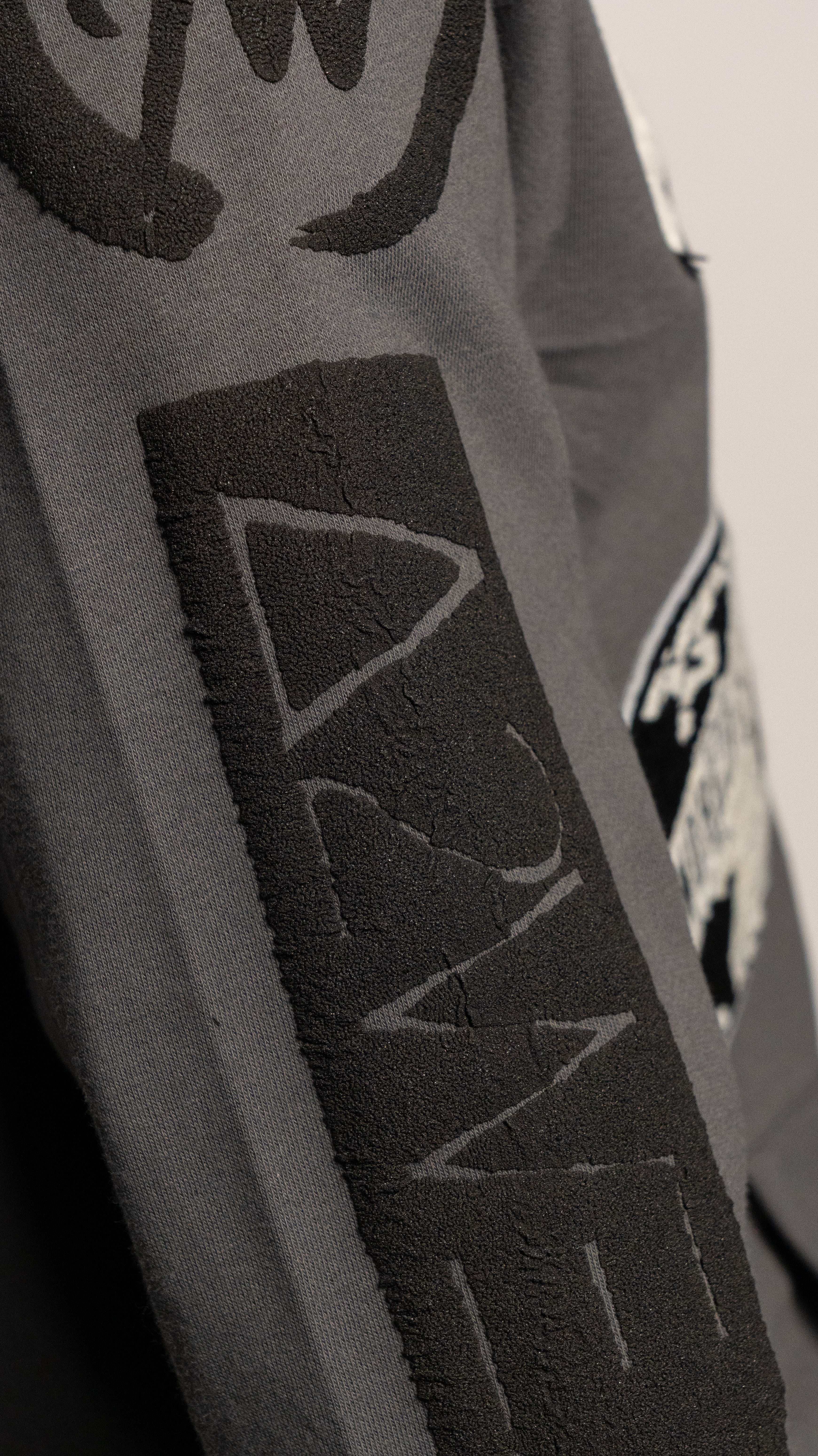 Close-up of a gray jacket with Art to wear logo on a plain background