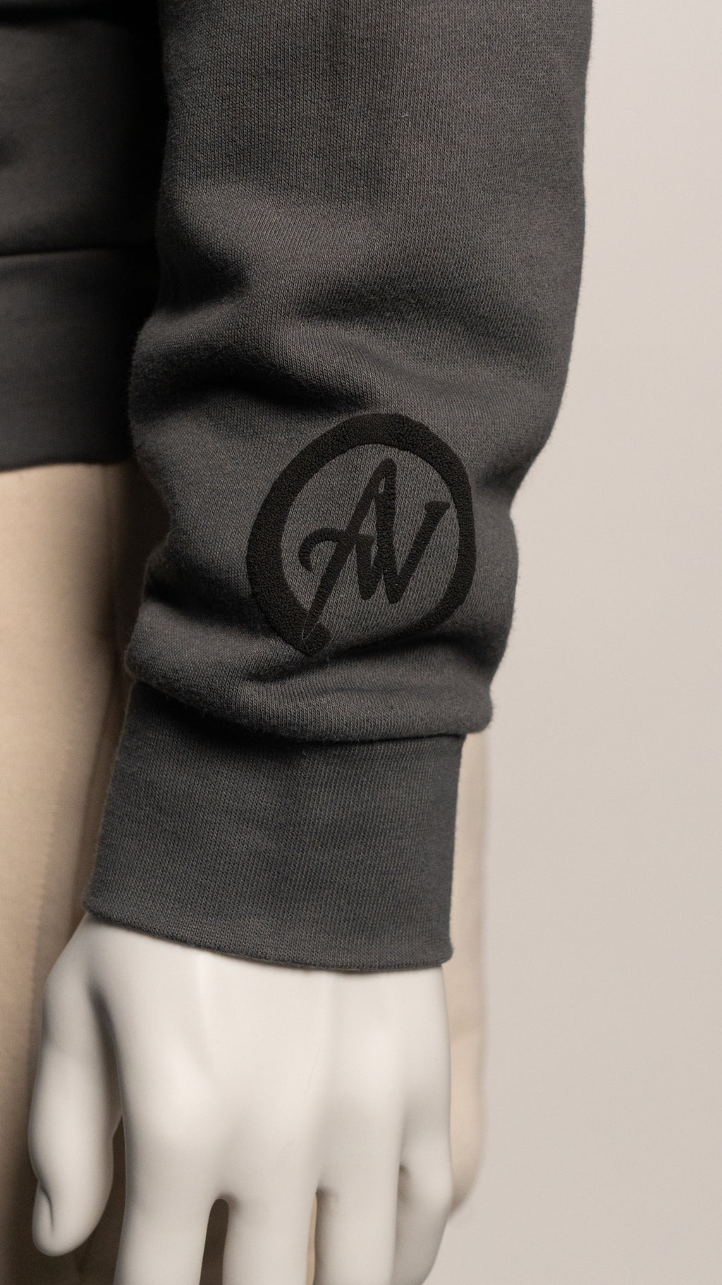 Dark gray sweatshirt sleeve with a logo on a neutral background