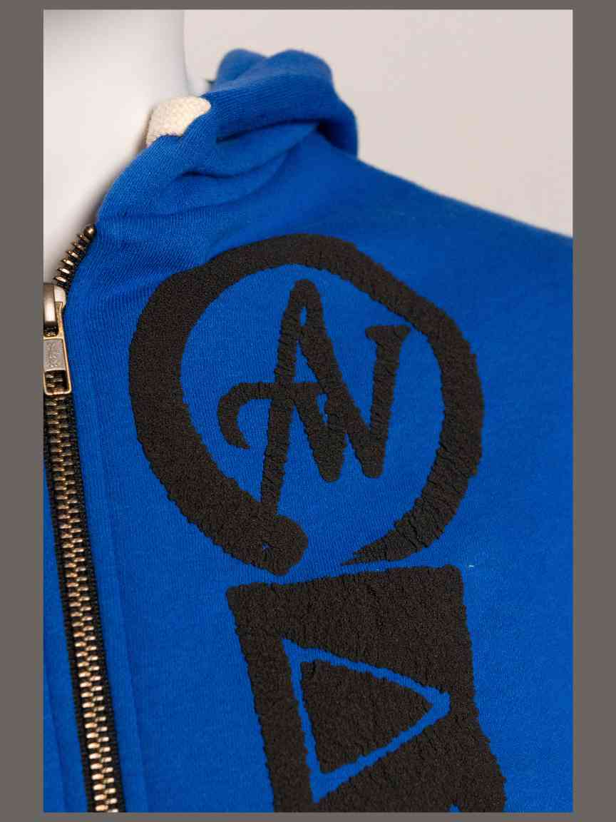 Blue jacket with black logo featuring letters 'AW' by a pen surrounded by a circle