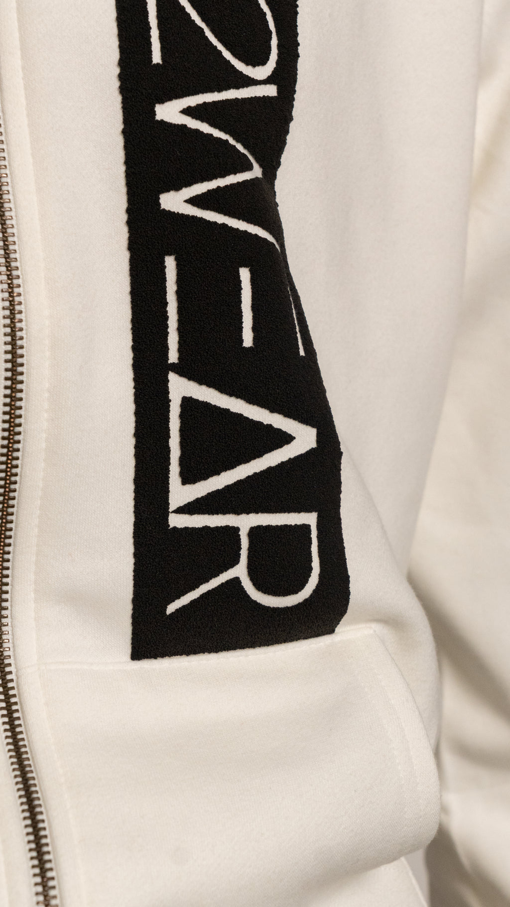 Close-up of a cream jacket with a black logo on the sleeve.