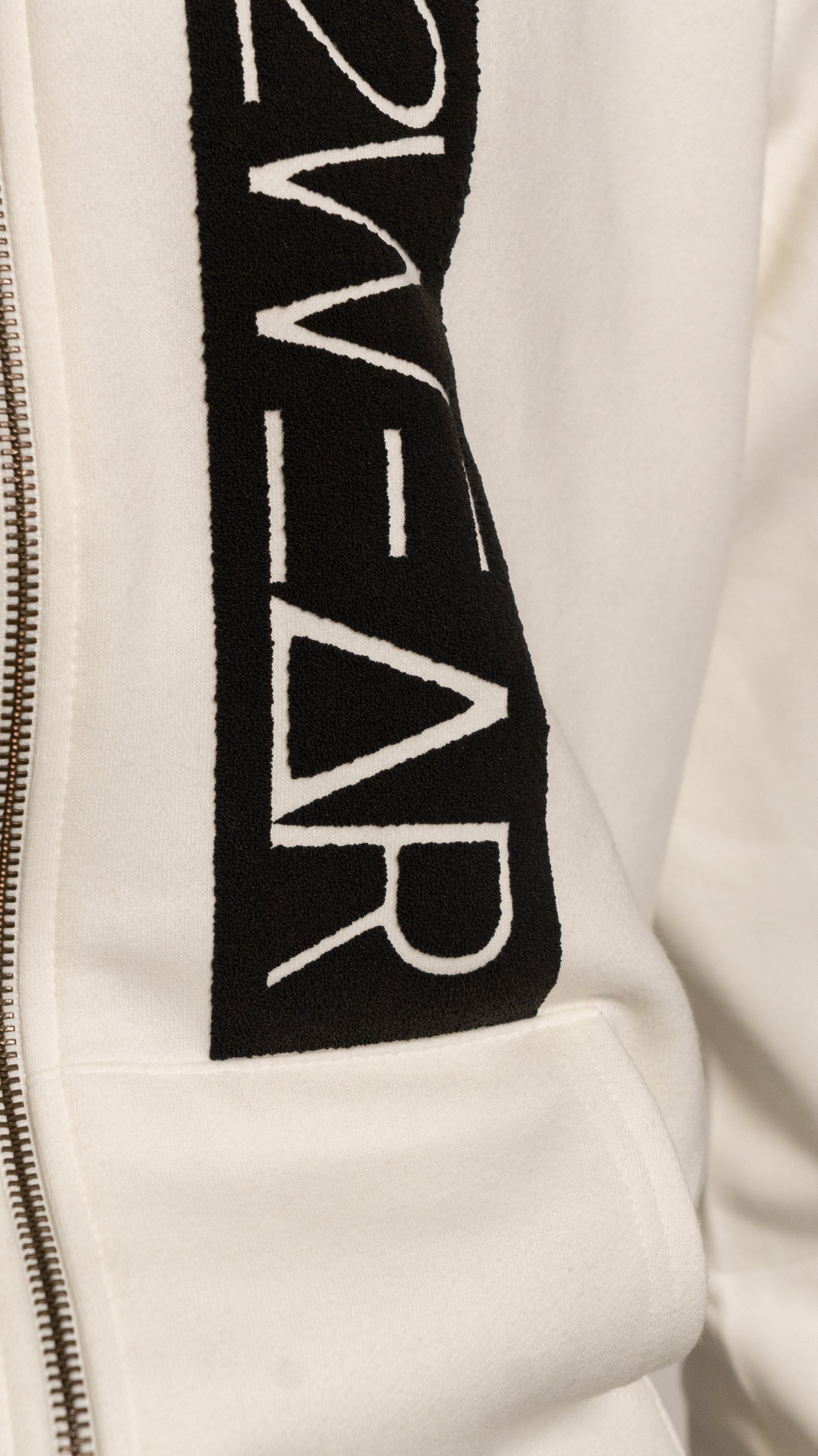 Close-up of a cream jacket with a black logo on the sleeve.